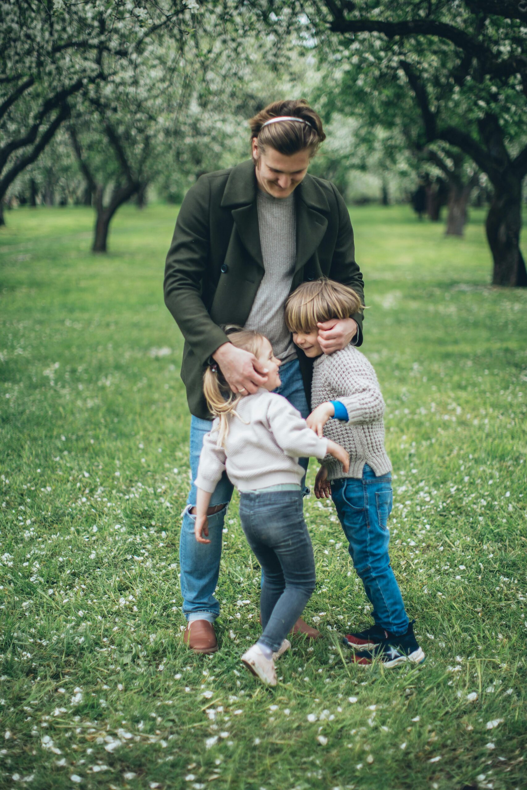 A father lovingly embraces his children in a blooming spring orchard.